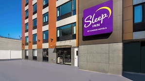 A Sleep IN by Choice Hotels building with a modern facade, large windows, and a prominent purple sign. - Sleep Inn Bronx - Soundview (Bronx)