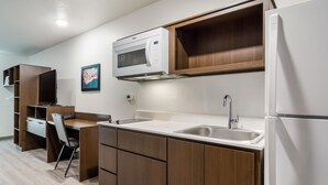Cocina compacta con armarios de madera, microondas, lavabo y refrigerador.