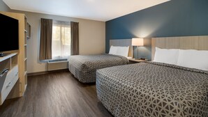 Habitación de hotel con dos camas, televisor, escritorio con cajones, ventana con cortinas y lámpara en la mesita de noche.