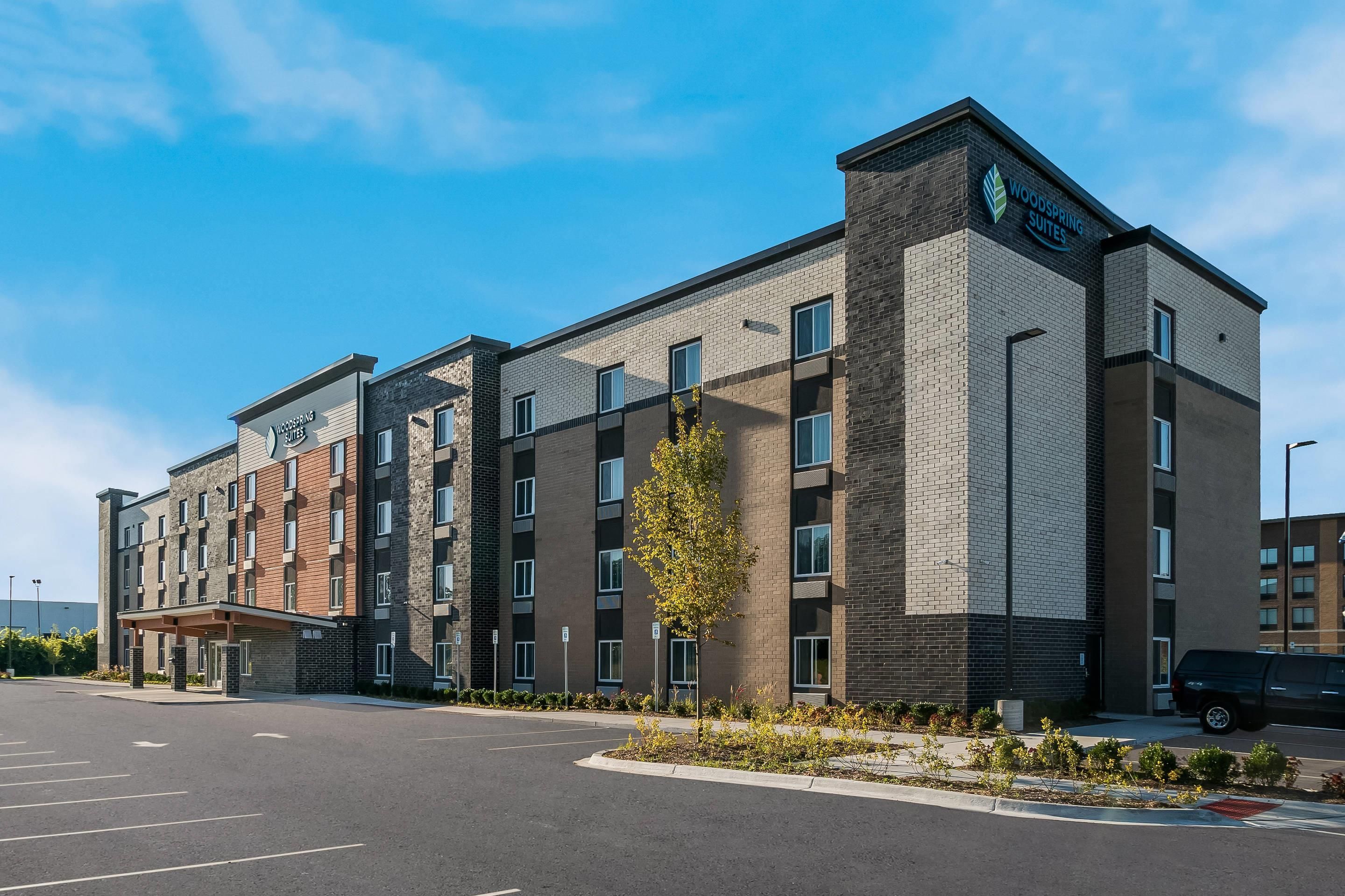A multi-story hotel with a modern brick facade, a parking lot in front, and a clear sky.
