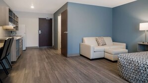Una habitación moderna con kitchenette, un sofá, una cama y una puerta que da a otra habitación.