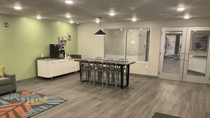 A modern kitchen with a dining area, a coffee machine, and a refrigerator. - Woodspring Suites Dearborn - Detroit (Dearborn)