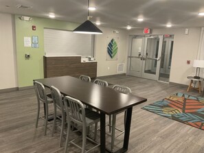 A conference room with a long table, chairs, a patterned rug, and a modern pendant light. - Woodspring Suites Dearborn - Detroit (Dearborn)