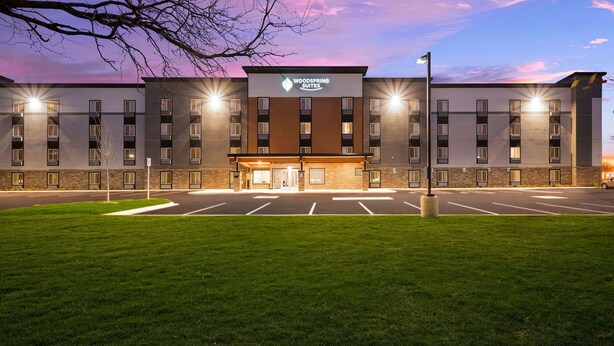 A multi-story hotel with a modern design, featuring a central entrance and a parking lot in front. - Woodspring Suites Dearborn - Detroit (Dearborn)