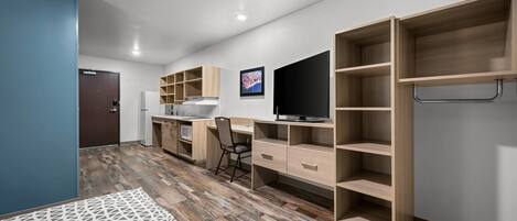A modern, compact room with a kitchenette, a flat-screen TV, and built-in shelving.