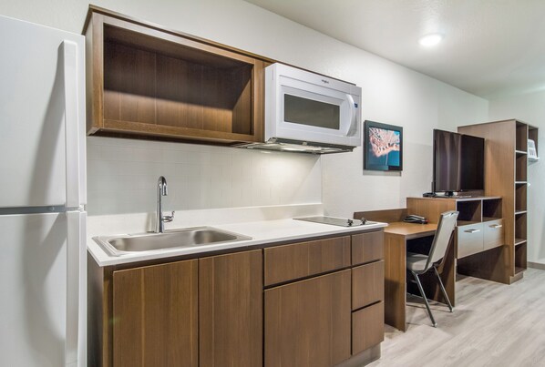 A compact kitchen with a built-in microwave, a sink, and wooden cabinets. - Woodspring Suites Dearborn - Detroit (Dearborn)