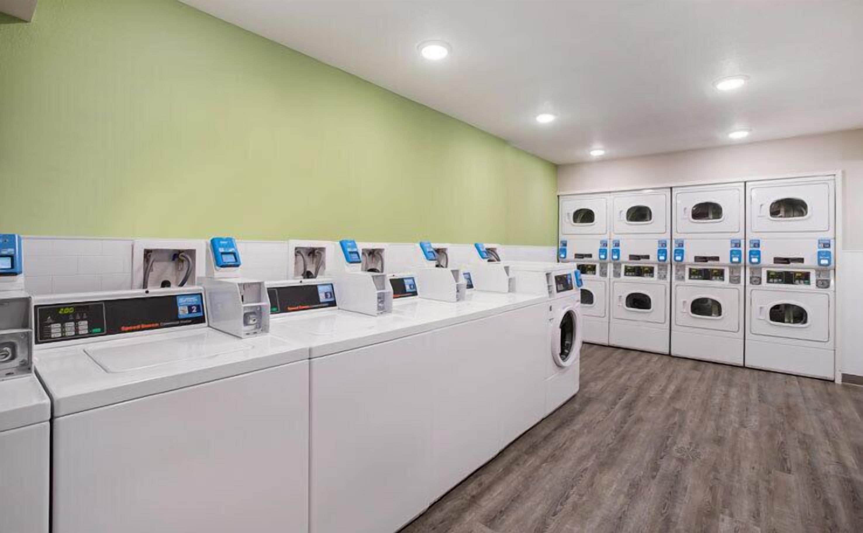 A laundry facility with multiple washing machines and dryers, a control panel, and a green wall.