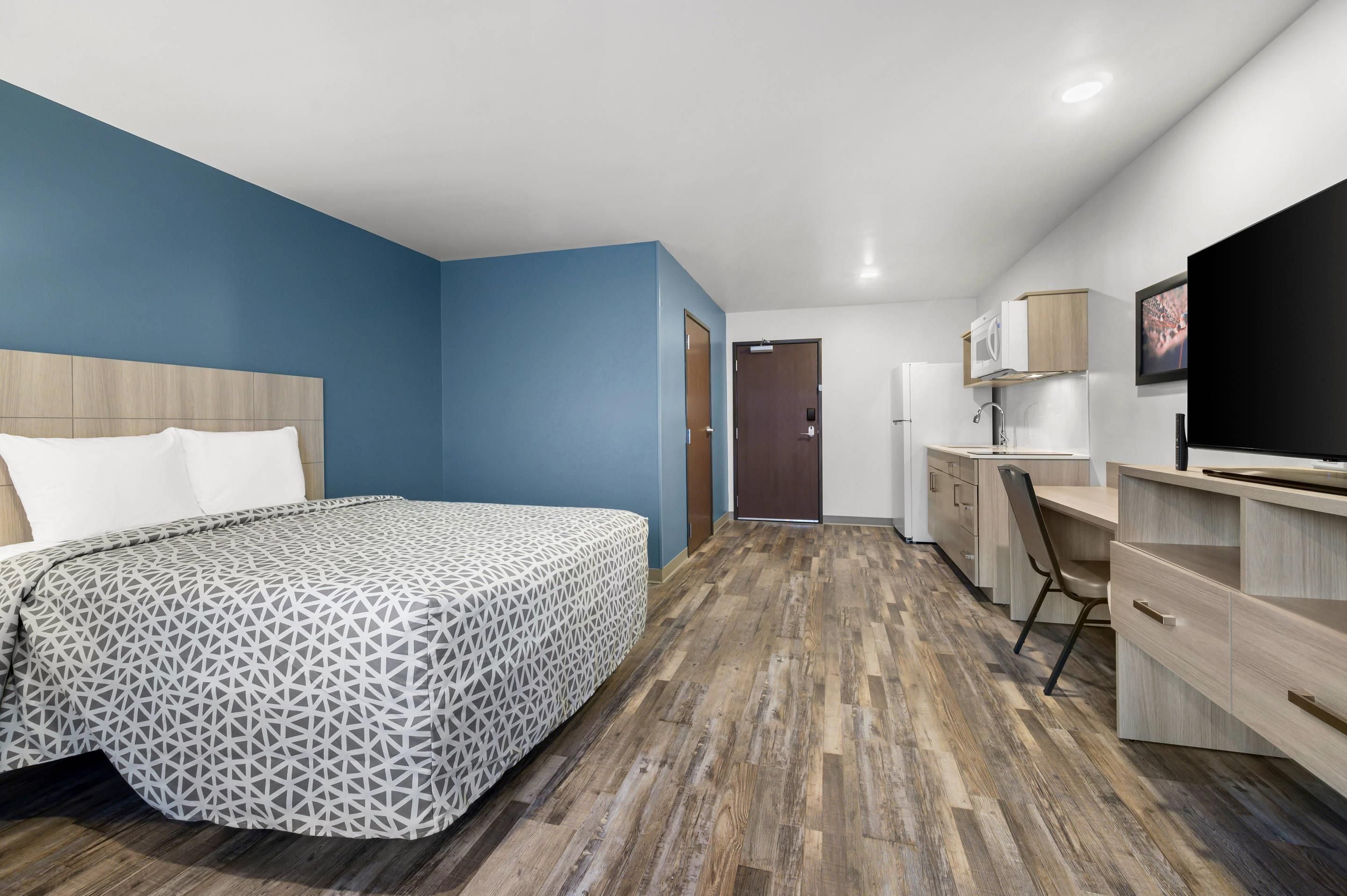 A hotel room with a bed, a desk, a chair, a television, and a door.