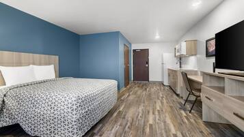 A hotel room with a bed, a desk, a chair, a television, and a door.