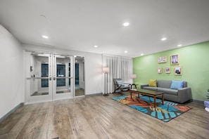 A modern living room with a grey sofa, a coffee table, and a colorful rug. - Woodspring Suites Dearborn - Detroit (Dearborn)