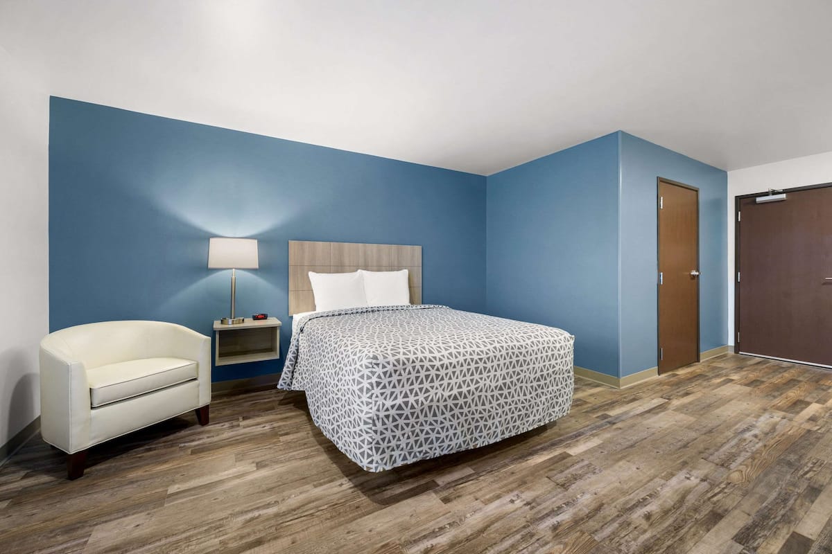 A bedroom with a bed, a bedside table, a lamp, a chair, and a wardrobe.