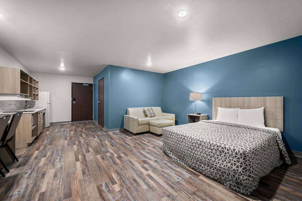 A modern bedroom with a large bed, a sofa, a desk, and a kitchenette.