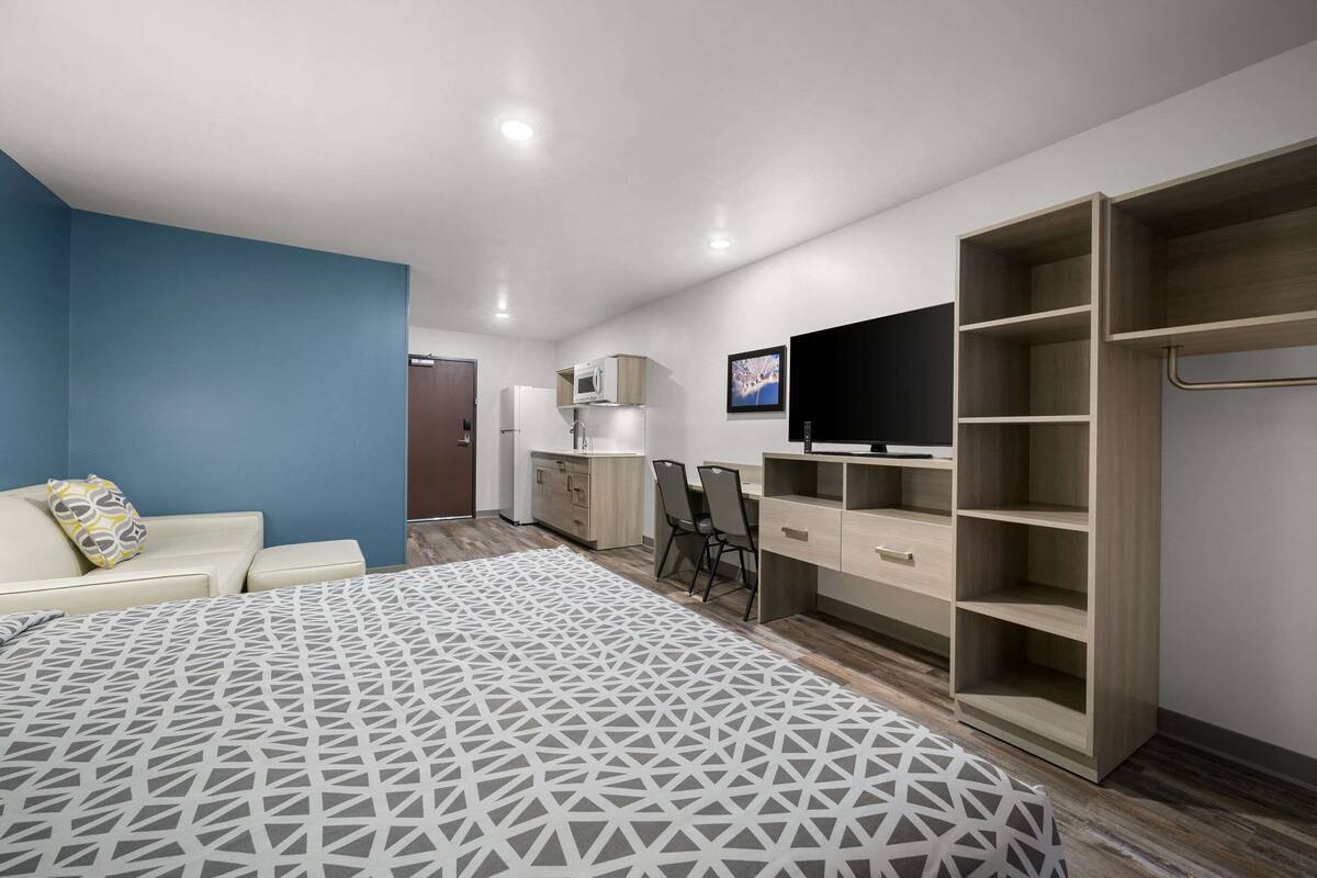 A modern bedroom with a bed, a desk, a TV, a wardrobe, and a microwave.