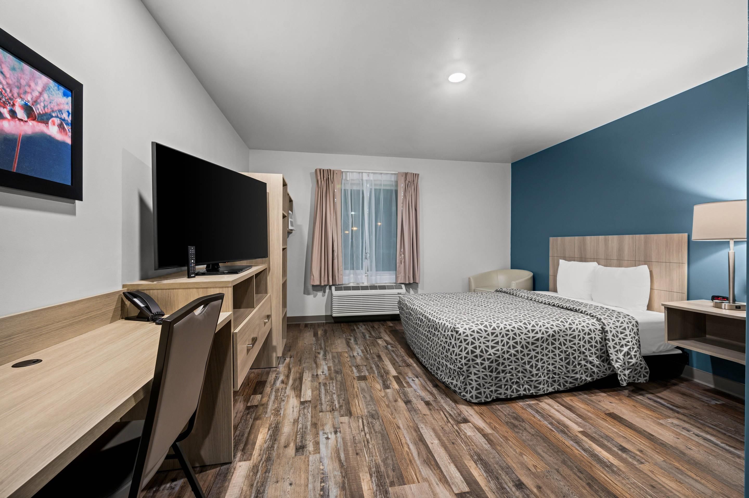 A hotel room with a bed, desk, chair, TV, and a window with curtains.