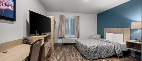 A hotel room with a bed, desk, chair, TV, and a window with curtains.
