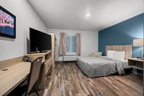 A hotel room with a bed, desk, chair, TV, and a window with curtains. - Woodspring Suites Dearborn - Detroit (Dearborn)
