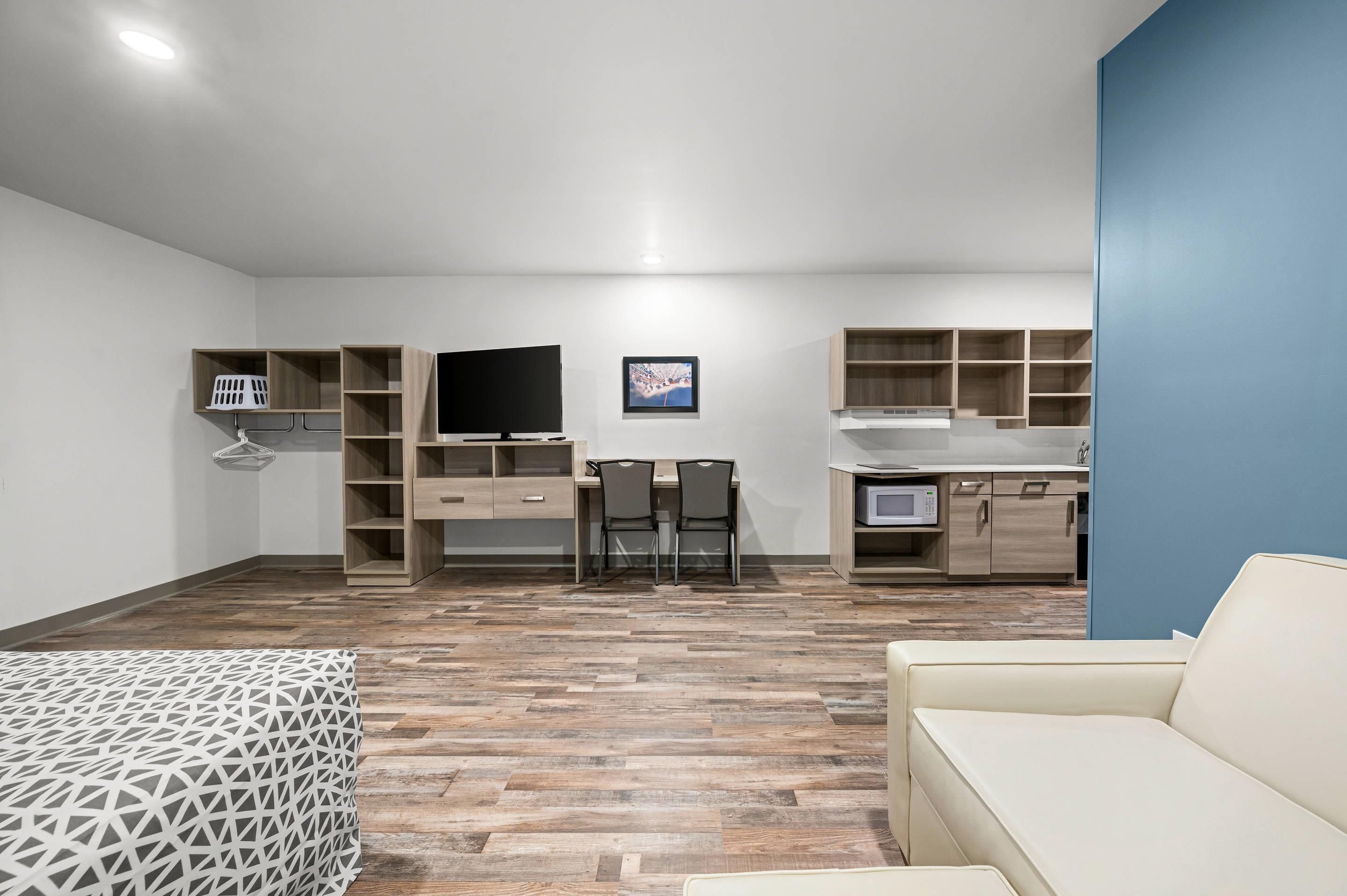 A modern, well-lit room with a flat-screen TV, a dining table with chairs, a sofa, and built-in wooden shelving.