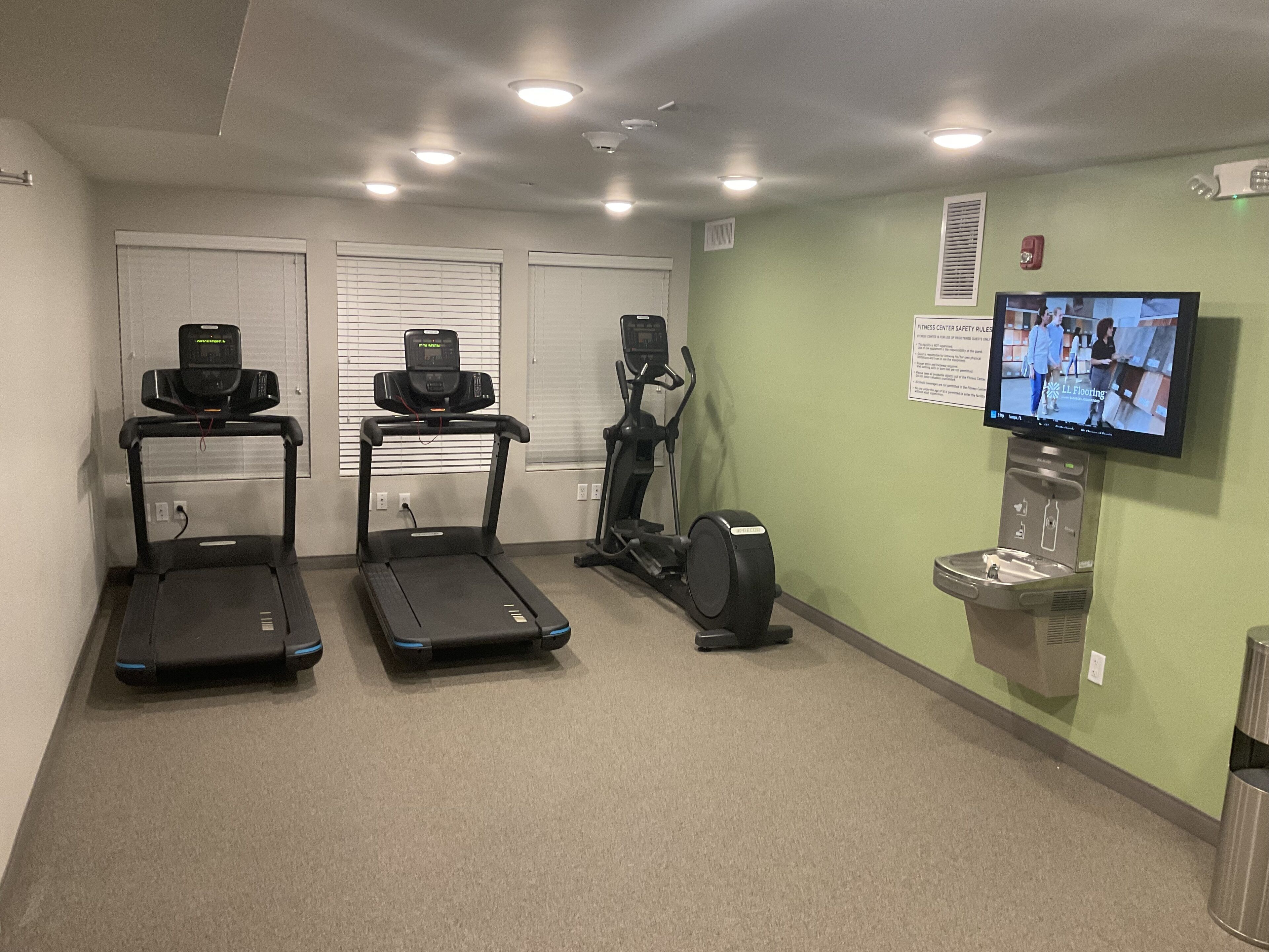 Un gimnasio con cintas de correr, una elíptica y un televisor mostrando un programa de ejercicios.