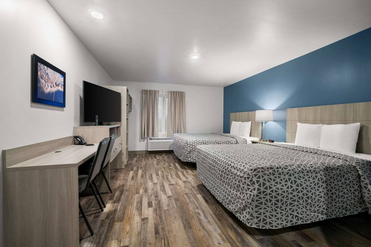A hotel room with a desk, two beds, a TV, and a window with curtains.