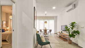 Una sala moderna con comedor, un sillón verde, un televisor y una planta grande.