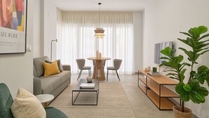 Una sala de estar moderna con sofá, mesa de centro, mesa de comedor, sillas y una planta grande.