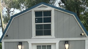 A small, single-story building with a white door, two windows, and a blue roof.