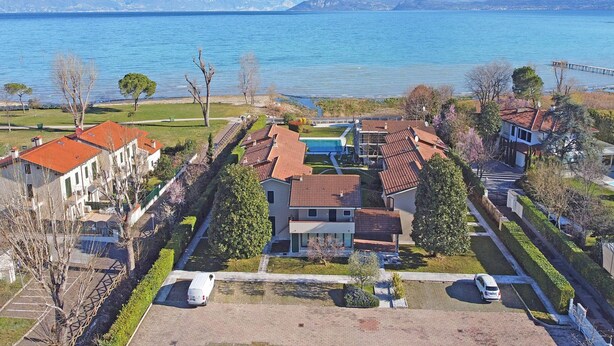 A residential area with houses, a swimming pool, and a view of a lake with mountains in the background. - Il Porticciolo P1 12 by Wonderful Italy (Sirmione)