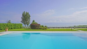A clear blue swimming pool with a view of the sea and a well-maintained garden with hedges and a tree. - Il Porticciolo P1 12 by Wonderful Italy (Sirmione)