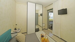 A small, compact room with a bed, a desk with a laptop, a tray of breakfast, and a TV mounted on the wall. - Il Porticciolo P1 12 by Wonderful Italy (Sirmione)