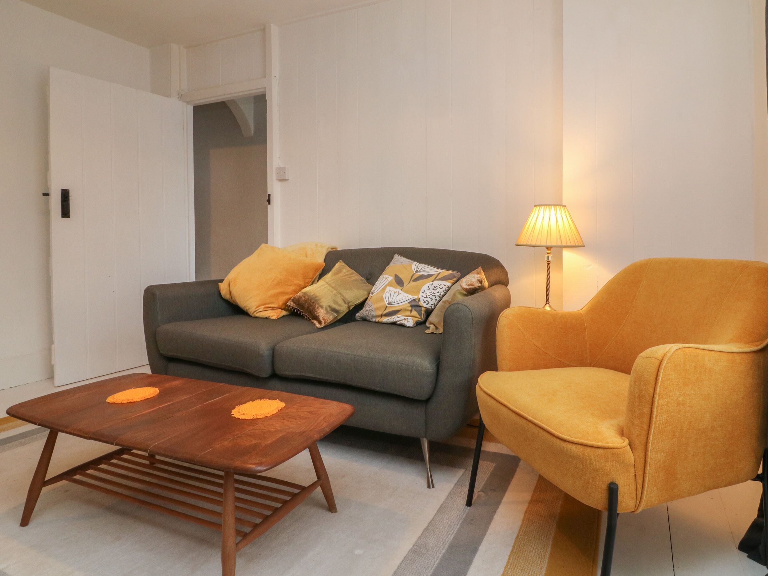 Una sala de estar con un sofá, una silla, una mesita de centro y una lámpara.