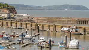 A marina with boats docked, a rocky breakwater, and a view of the sea and distant hills. - Oyster Catchers (Watchet)