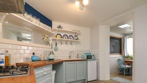 A compact kitchen with white cabinets, a wooden countertop, a gas stove, a microwave, and a small refrigerator. - Oyster Catchers (Watchet)