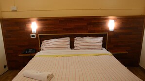 Camera d'albergo con testiera in legno, due abat-jour, un telefono e un letto rifatto con lenzuola a righe.