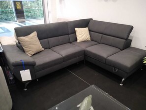 A dark grey sectional sofa with two beige cushions, a tag on the armrest, and a glass table with a dolphin figurine. - Albergo Royal Genova (Genoa)
