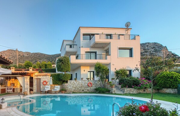 Un edificio moderno de varios pisos con piscina, muros de piedra y montañas al fondo.