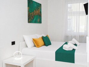 Ein Hotelzimmer mit einem weißen Bett, einer grünen Tagesdecke und einem weißen Nachttisch mit einem Ringlicht.