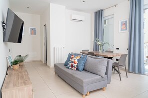 Ein modernes Wohnzimmer mit grauem Sofa, einem Holztisch, einem Flachbildfernseher und einem Essbereich mit Holztisch und Stühlen.