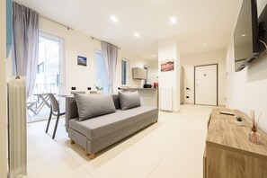 A modern living room with a sofa, a wooden side table, a TV, and a kitchen area in the background.