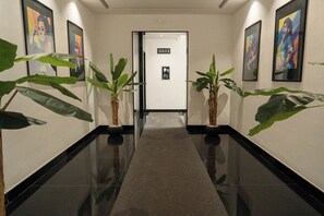 A hallway with a polished floor, potted plants, and framed artwork on the walls.