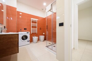 A modern bathroom with a washing machine, two sinks, a glass shower enclosure, and a wooden vanity.