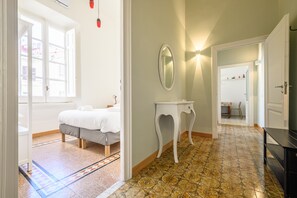 A bedroom with a bed, a bedside table, a mirror, and a view of a hallway.