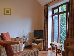 Sala de estar con muebles de mimbre, un televisor y una ventana con cortinas.