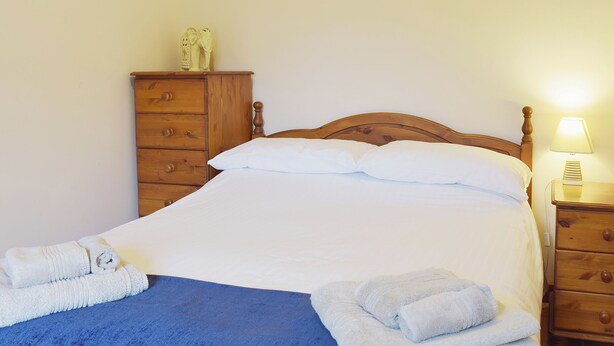 Un lit bien fait, avec du linge de lit blanc et des couvertures bleues, des meubles en bois et une table de chevet avec une lampe.