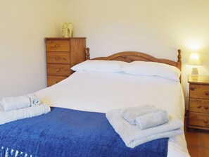 Una cama bien hecha con ropa de cama blanca y ropa de cama azul, muebles de madera y una mesita de noche con una lámpara.