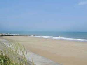 Une plage avec une promenade en béton et une jetée en bois qui s’avance dans l’eau.