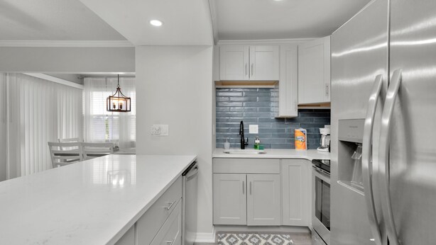 Una cocina moderna con muebles blancos, un refrigerador de acero inoxidable y encimera de mármol.