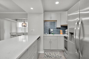 Una cocina moderna con muebles blancos, un refrigerador de acero inoxidable y encimera de mármol.