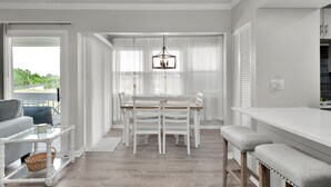 Un comedor moderno y bien iluminado con una mesa y sillas blancas, una lámpara colgante y vistas amplias a través de grandes ventanales.