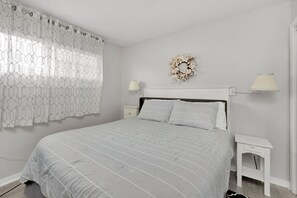 Une chambre à coucher avec un grand lit, des murs blancs, une couronne décorative et deux lampes de chevet.