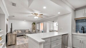 Una cocina moderna con una isla central, armarios blancos y un ventilador de techo.